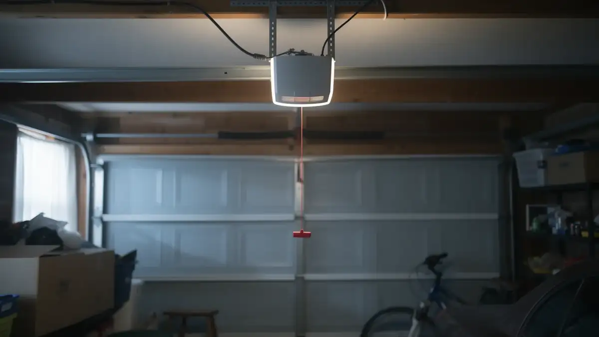 A white garage door opener hangs from the ceiling in a garage.